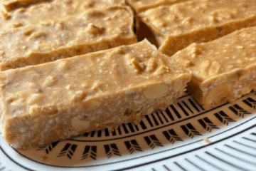 No-bake peanut butter bars cut into squares and arranged on a white plate, with visible bits of roasted peanuts and shredded coconut. The bars have a golden, slightly textured appearance and are set against a clean, natural background.