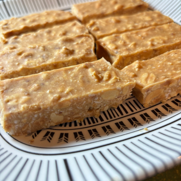 No-bake peanut butter bars cut into squares and arranged on a white plate, with visible bits of roasted peanuts and shredded coconut. The bars have a golden, slightly textured appearance and are set against a clean, natural background.