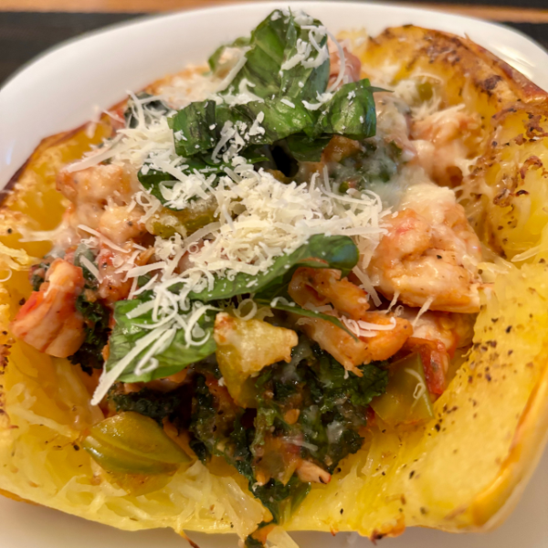 Stuffed spaghetti squash halves filled with chicken, tomatoes, kale, and topped with Parmesan and fresh basil.