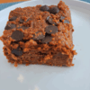 Grain-free chocolate zucchini cake topped with melted and cooled chocolate chips, sliced and served on a white plate.