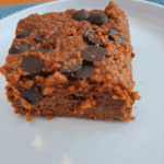 Grain-free chocolate zucchini cake topped with melted and cooled chocolate chips, sliced and served on a white plate.
