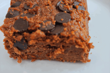 Grain-free chocolate zucchini cake topped with melted and cooled chocolate chips, sliced and served on a white plate.