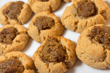SCD pistachio-date thumbprint cookies on a white plate, featuring golden almond flour cookie bases filled with a rustic, textured date and pistachio mixture.