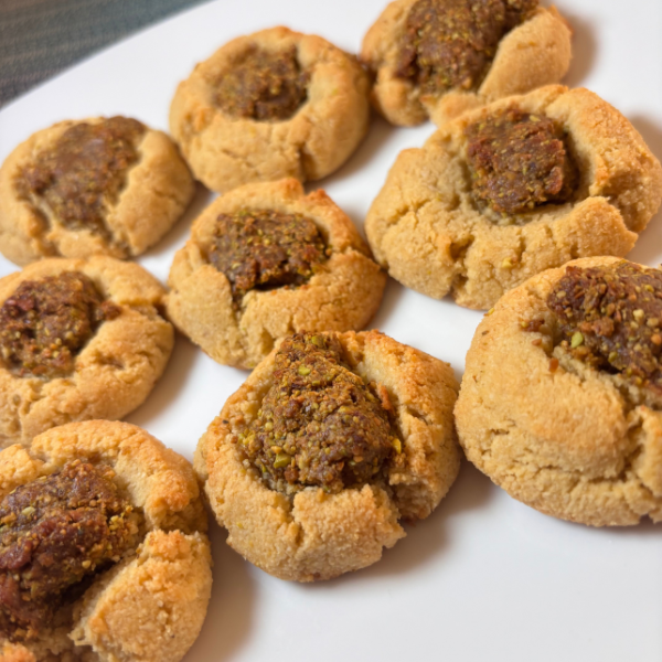 SCD pistachio-date thumbprint cookies on a white plate, featuring golden almond flour cookie bases filled with a rustic, textured date and pistachio mixture.
