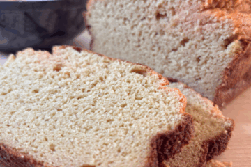 Sliced loaf of golden-brown red lentil bread on a wooden surface, with a soft, tender crumb and a bowl of red lentils in the background.