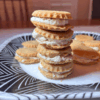 A stack of small vanilla cream sandwich cookies on a patterned plate.
