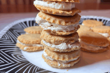 A stack of small vanilla cream sandwich cookies on a patterned plate.