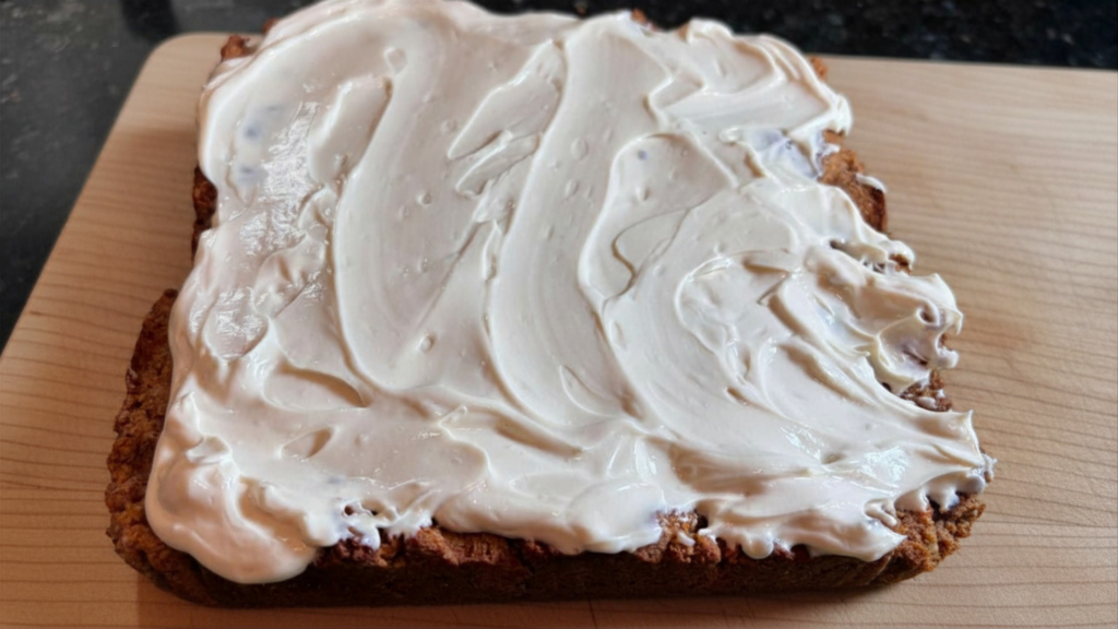 Uncut SCD carrot cake bar on a wooden cutting board covered in thick swirled yogurt cream cheese frosting