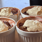 Four white ramekins of strawberry rhubarb crisp topped with dollops of SCD yogurt made with heavy cream, served on a wooden surface.