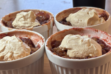 Four white ramekins of strawberry rhubarb crisp topped with dollops of SCD yogurt made with heavy cream, served on a wooden surface.